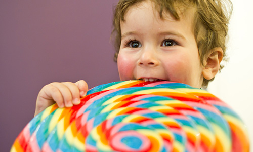 Kleiner Junge beißt mit gesunden Zähnen in einen Lolli und freut sich bei der Zahnprophylaxe beim Zahnarzt in Frechen.
