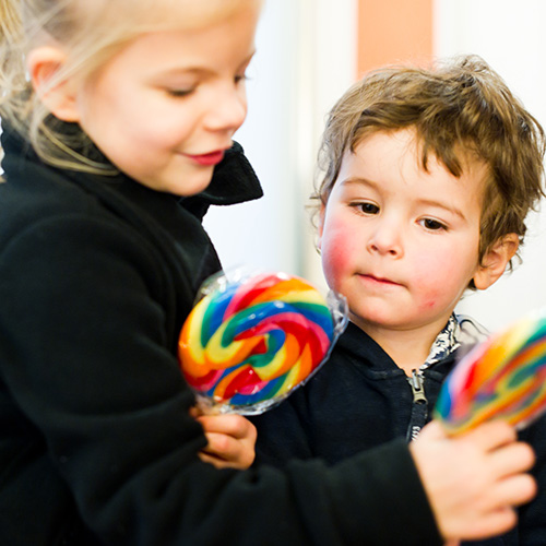 Kleines Mädchen und kleiner Junge halten Lutscher in der Hand und freuen sich über gesunde Kinderzähne in Frechen.